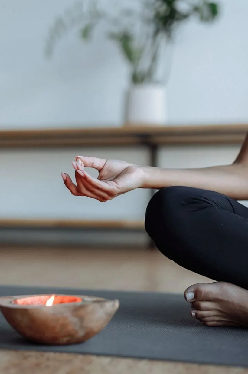 Seated pose with a hand resting in mudra beside a small bowl on a dark mat
