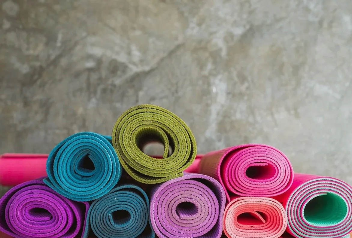 Rolled yoga mats in teal, green, pink and purple stacked against a stone wall